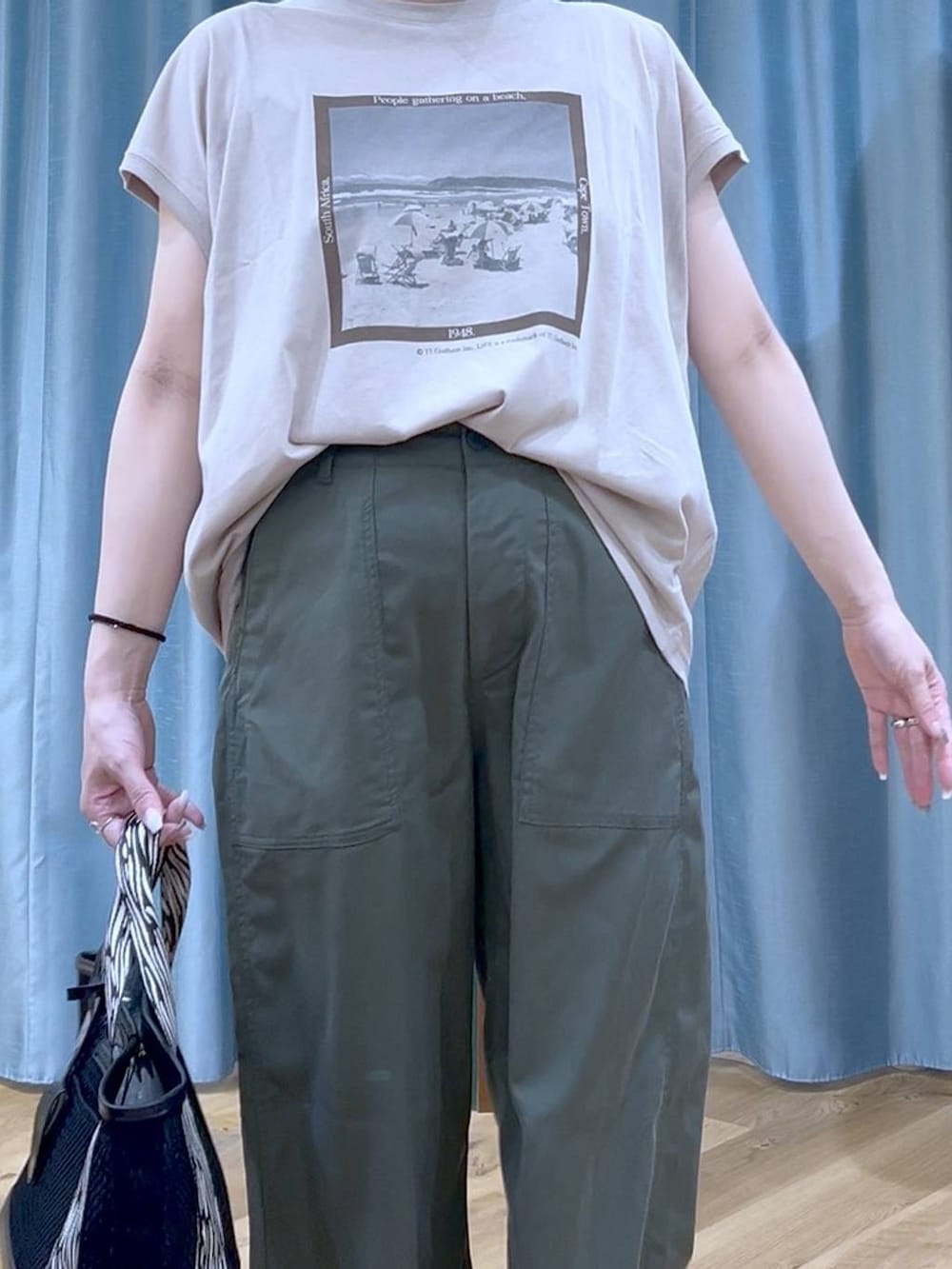 ブラック系のトートバッグ、ベージュ系のTシャツ/カットソー、グリーン系のチノパンツを着用したレディースの夏コーディネートの7枚目の写真