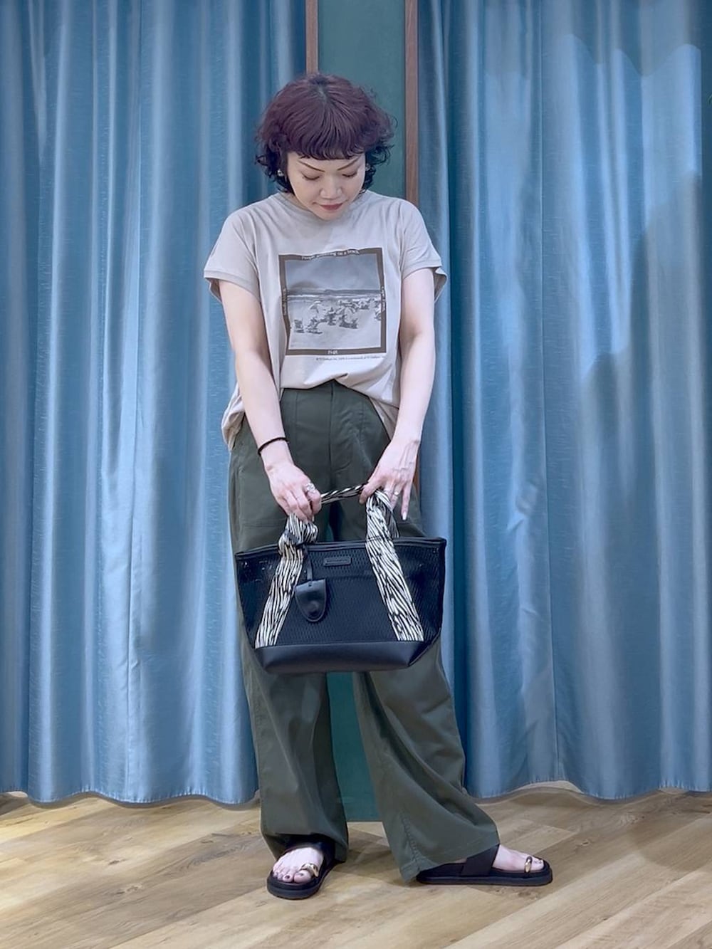 ブラック系のトートバッグ、ベージュ系のTシャツ/カットソー、グリーン系のチノパンツを着用したレディースの夏コーディネートの4枚目の写真