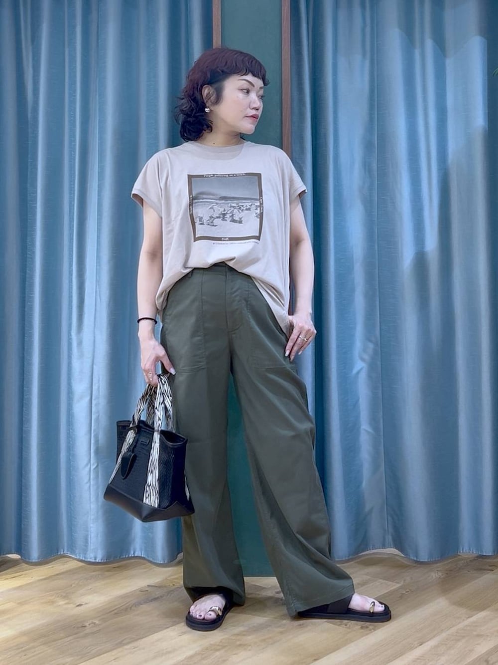 ブラック系のトートバッグ、ベージュ系のTシャツ/カットソー、グリーン系のチノパンツを着用したレディースの夏コーディネートの2枚目の写真