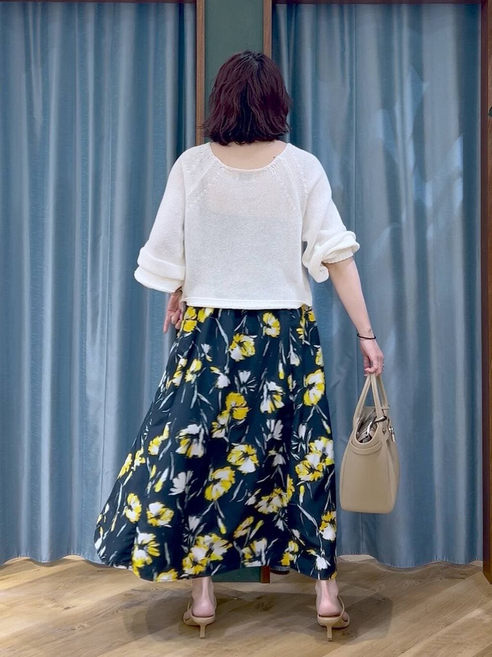 ホワイト系のニット/セーター、ブルー系のスカート、ベージュ系のハンドバッグを着用したレディースの春コーディネートの4枚目の写真