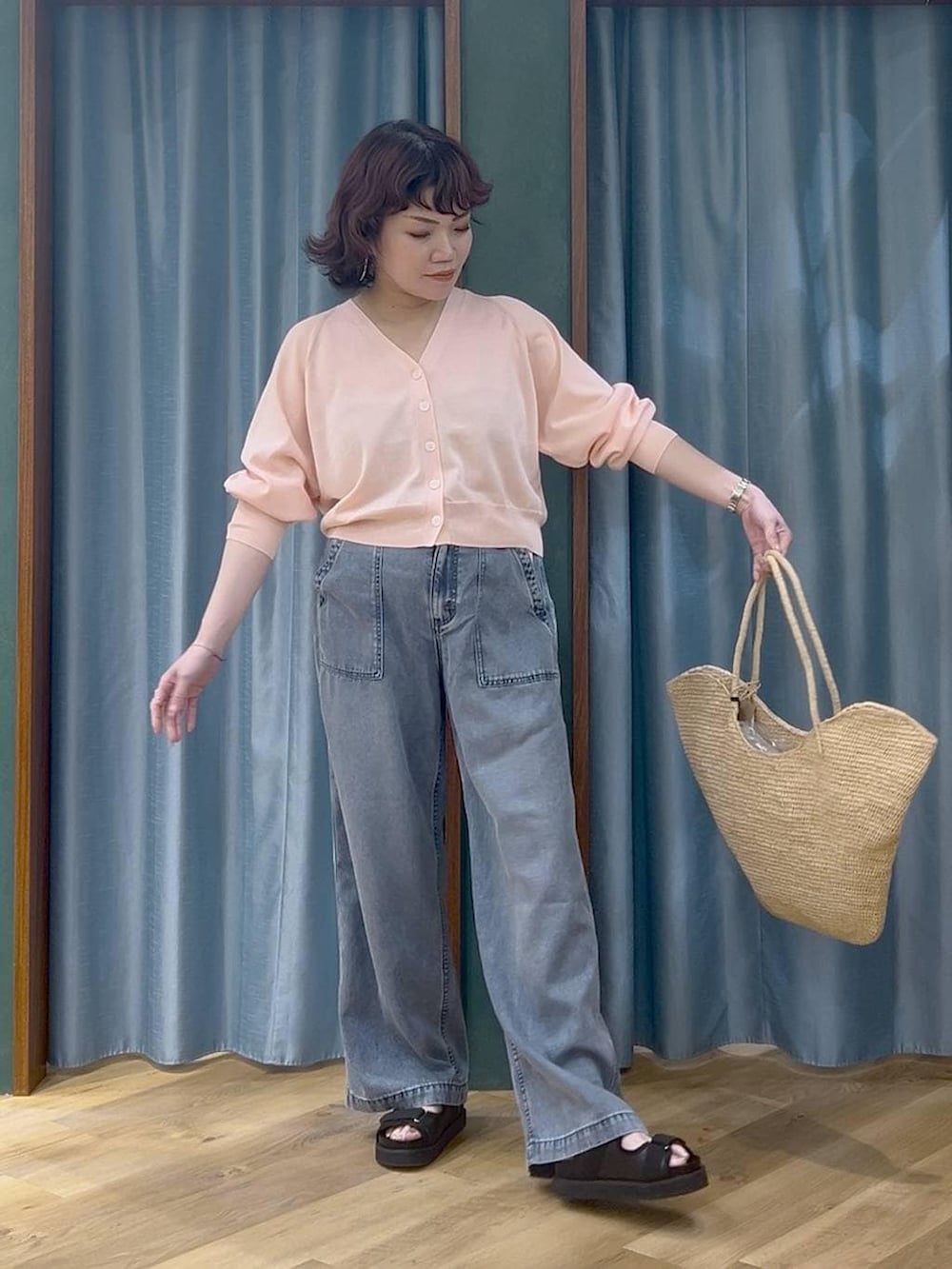 ブルー系のデニムパンツ、ピンク系のカーディガン/ボレロ、ベージュ系のかごバッグを着用したレディースの春コーディネートの2枚目の写真