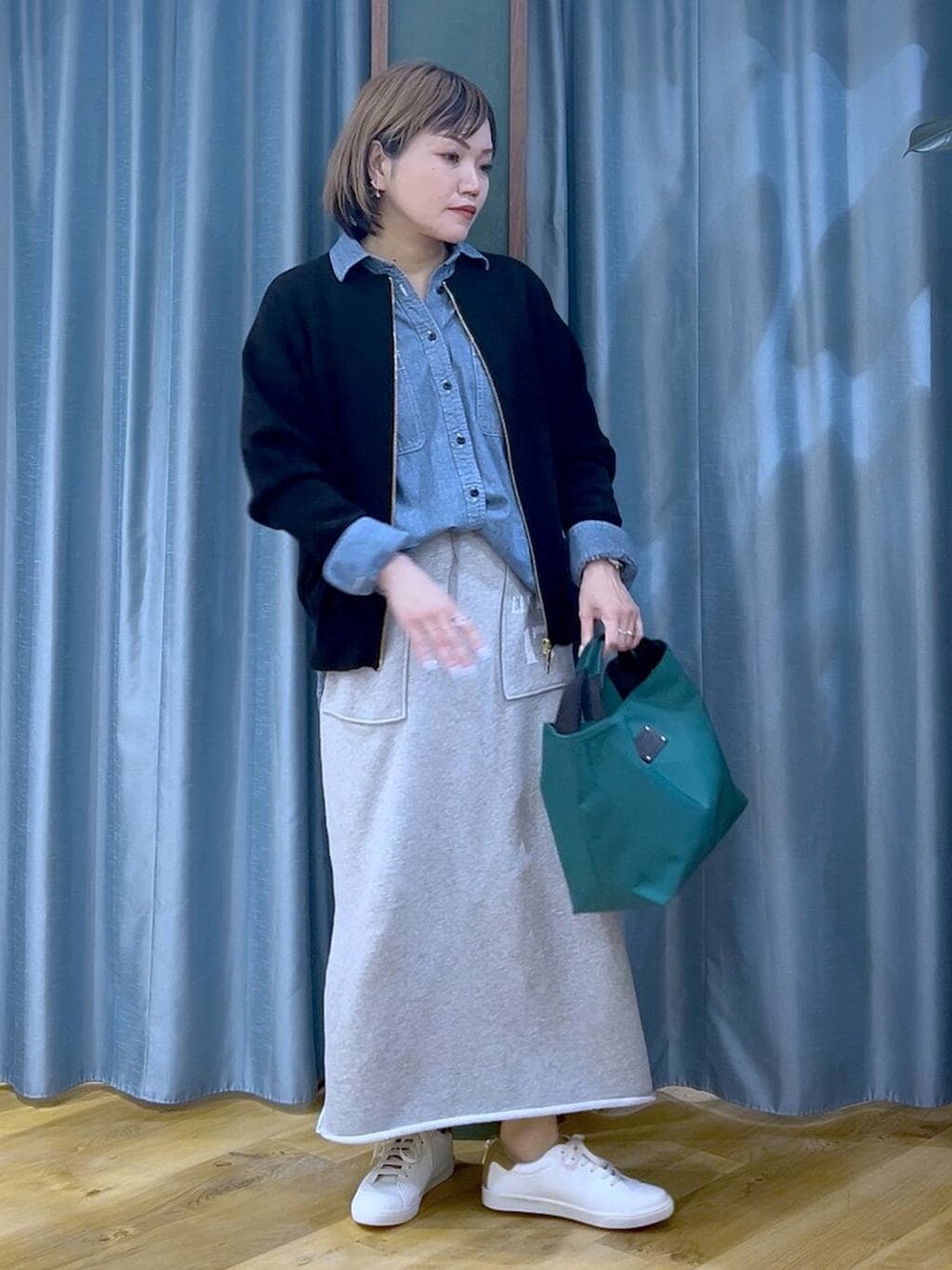 グリーン系のトートバッグ、ブラック系のカーディガン/ボレロ、グレー系のスカートを着用したレディースの冬コーディネートの2枚目の写真