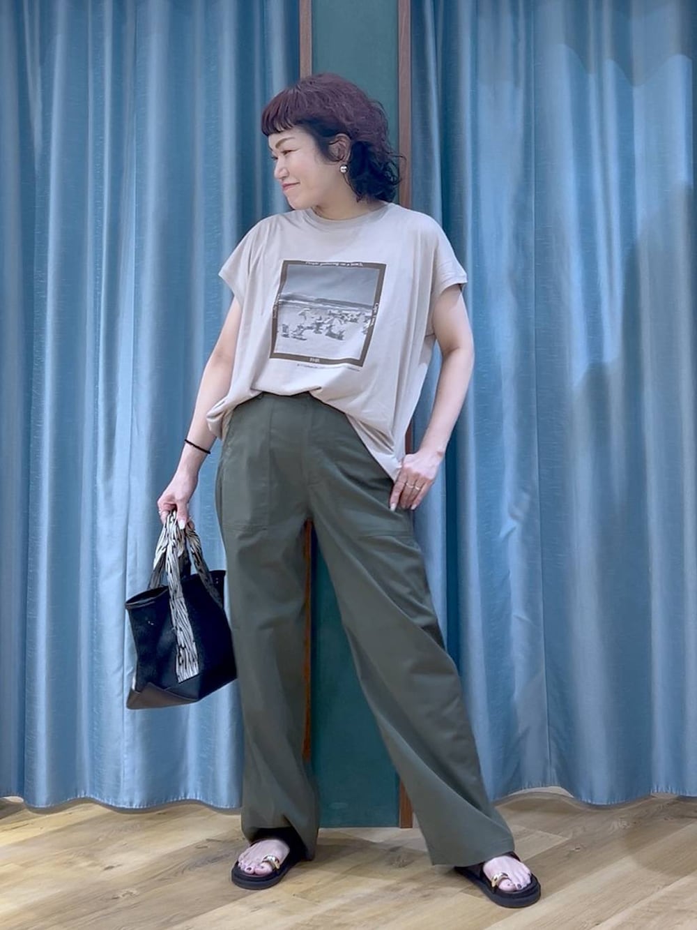 ブラック系のトートバッグ、ベージュ系のTシャツ/カットソー、グリーン系のチノパンツを着用したレディースの夏コーディネートの3枚目の写真