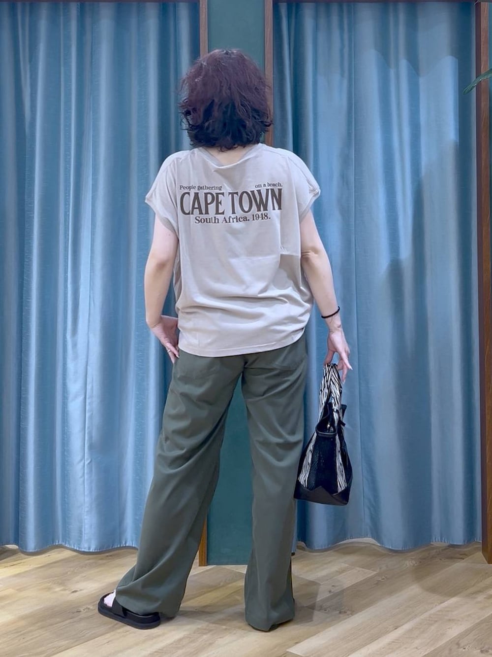 ブラック系のトートバッグ、ベージュ系のTシャツ/カットソー、グリーン系のチノパンツを着用したレディースの夏コーディネートの6枚目の写真