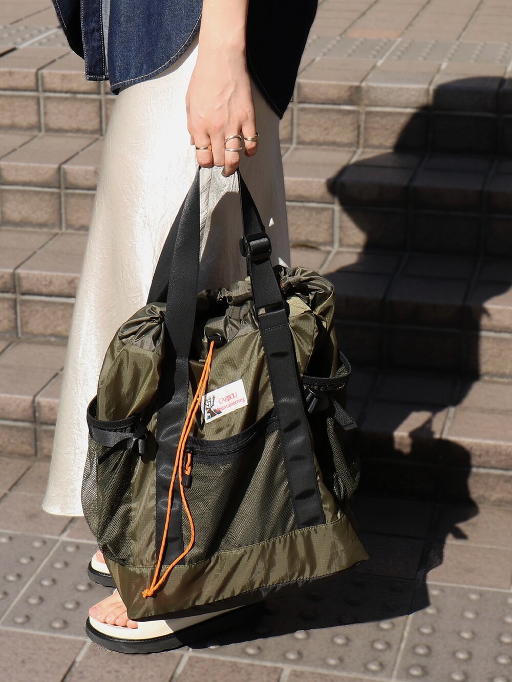 ブラック系のサンダル、ホワイト系のスカート、グリーン系のトートバッグを着用したレディースの春コーディネートの5枚目の写真