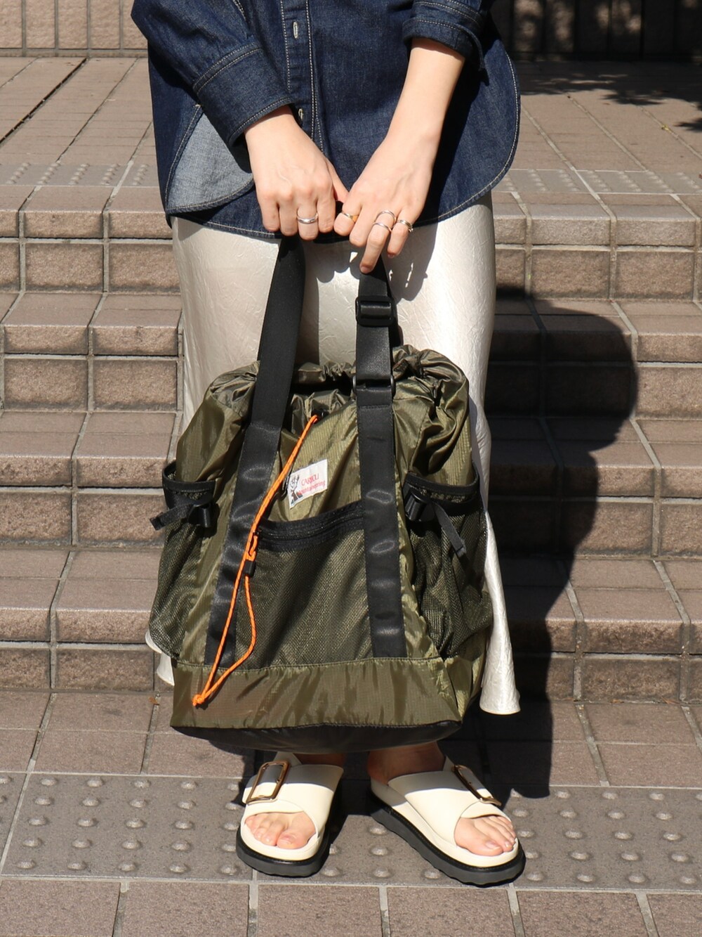 ブラック系のサンダル、ホワイト系のスカート、グリーン系のトートバッグを着用したレディースの春コーディネートの6枚目の写真