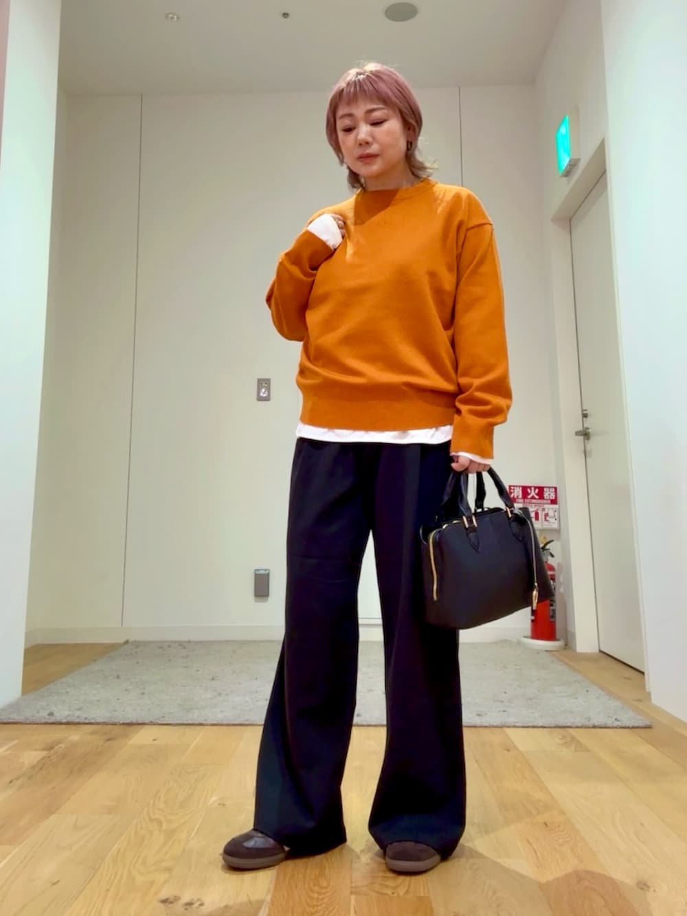 ブラック系のハンドバッグ、ホワイト系のTシャツ/カットソー、ベージュ系のステンカラーコートを着用したレディースの秋コーディネートの4枚目の写真