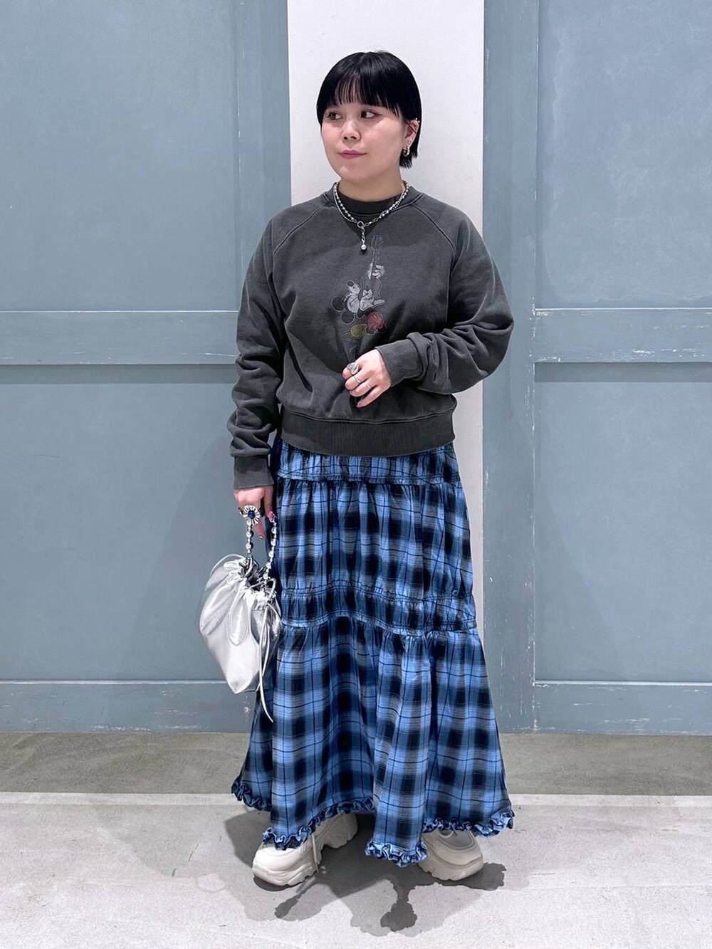 ブルー系のスカート、シルバー系のショルダーバッグ、ホワイト系のスニーカーを着用したレディースの夏コーディネートの2枚目の写真