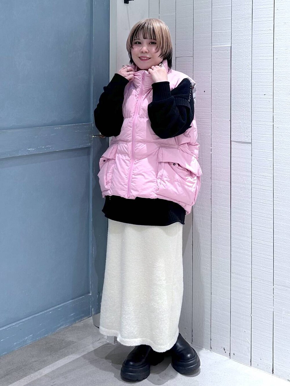 ピンク系のダウンベスト、ブラック系のTシャツ/カットソー、ホワイト系のスカートを着用したレディースの秋コーディネートの2枚目の写真