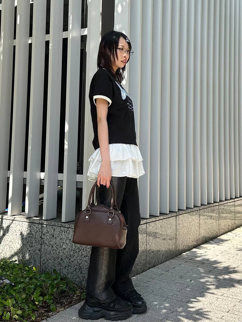 ブラック系のスニーカー、ブラック系のデニムパンツ、ブラウン系のショルダーバッグを着用したレディースの夏コーディネートの3枚目の写真