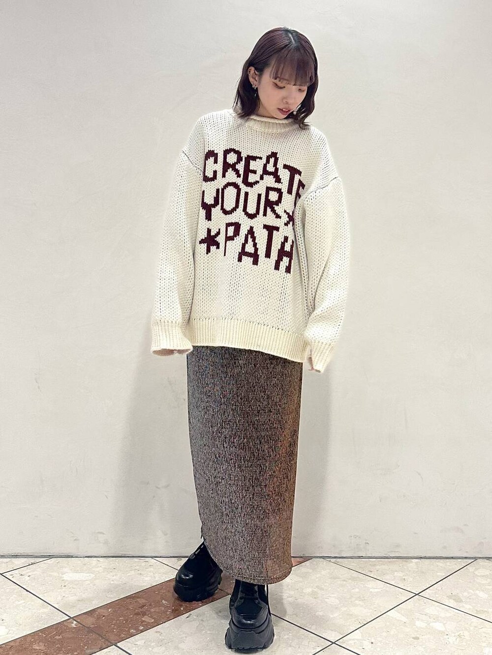 ブラック系のブーツ、ホワイト系のニット/セーター、ゴールド系のスカートを着用したレディースの冬コーディネートの2枚目の写真