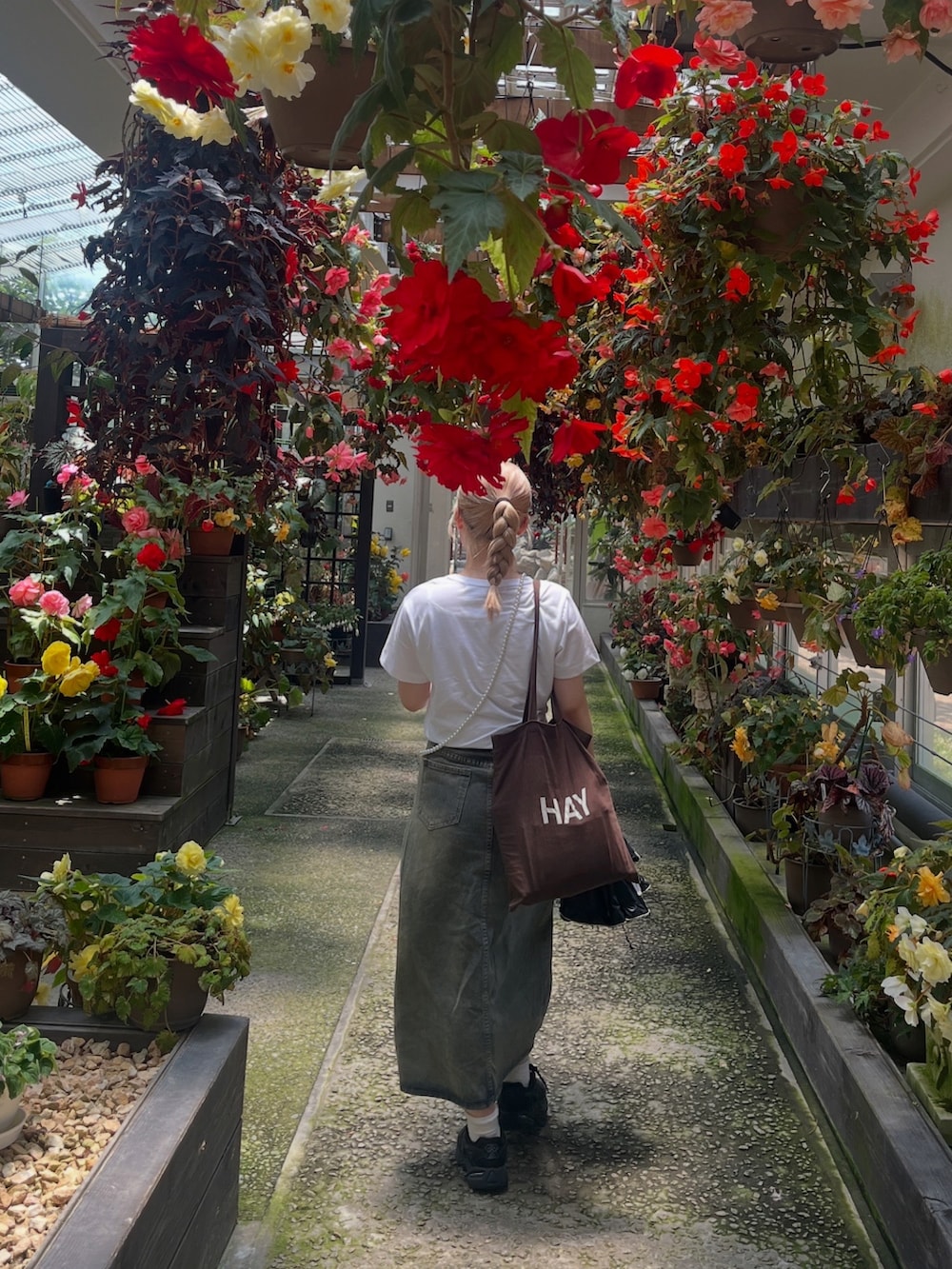 ブルー系のデニムスカート、ブラウン系のトートバッグ、ブラック系のスニーカーを着用したレディースの夏コーディネートの2枚目の写真