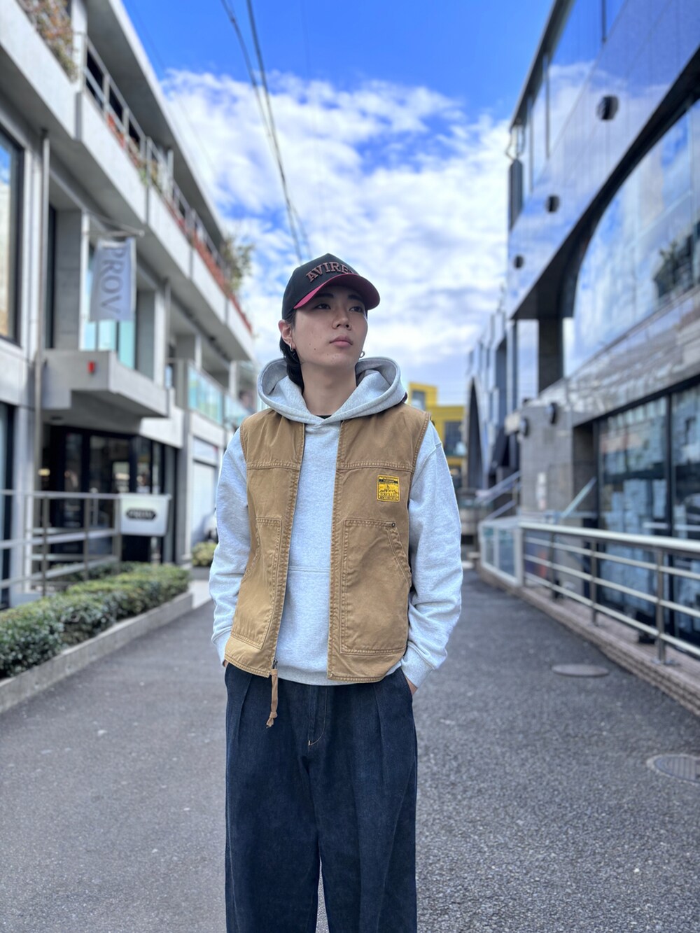 グレー系のパーカー、ベージュ系のベスト、レッド系のキャップを着用したメンズの冬コーディネートの3枚目の写真