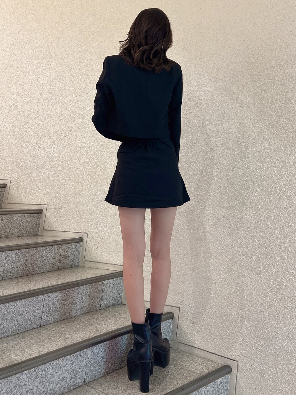 ブラック系のスカート、ブラック系のテーラードジャケット、ブラック系のブーツを着用したレディースの秋コーディネートの3枚目の写真