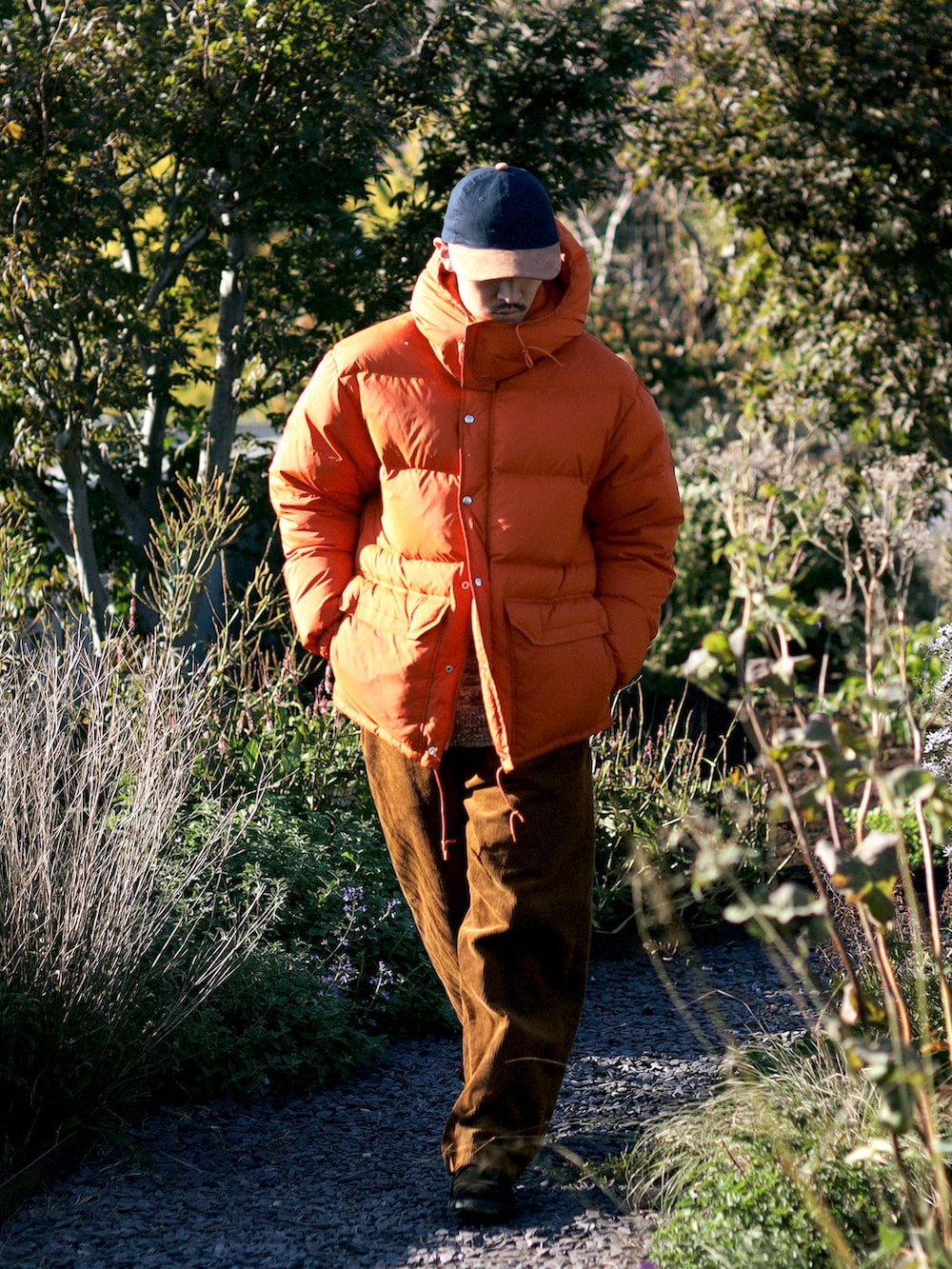 オレンジ系のダウンジャケット/コート、ブラウン系のその他パンツ、ブルー系のキャップを着用したメンズの冬コーディネートの2枚目の写真