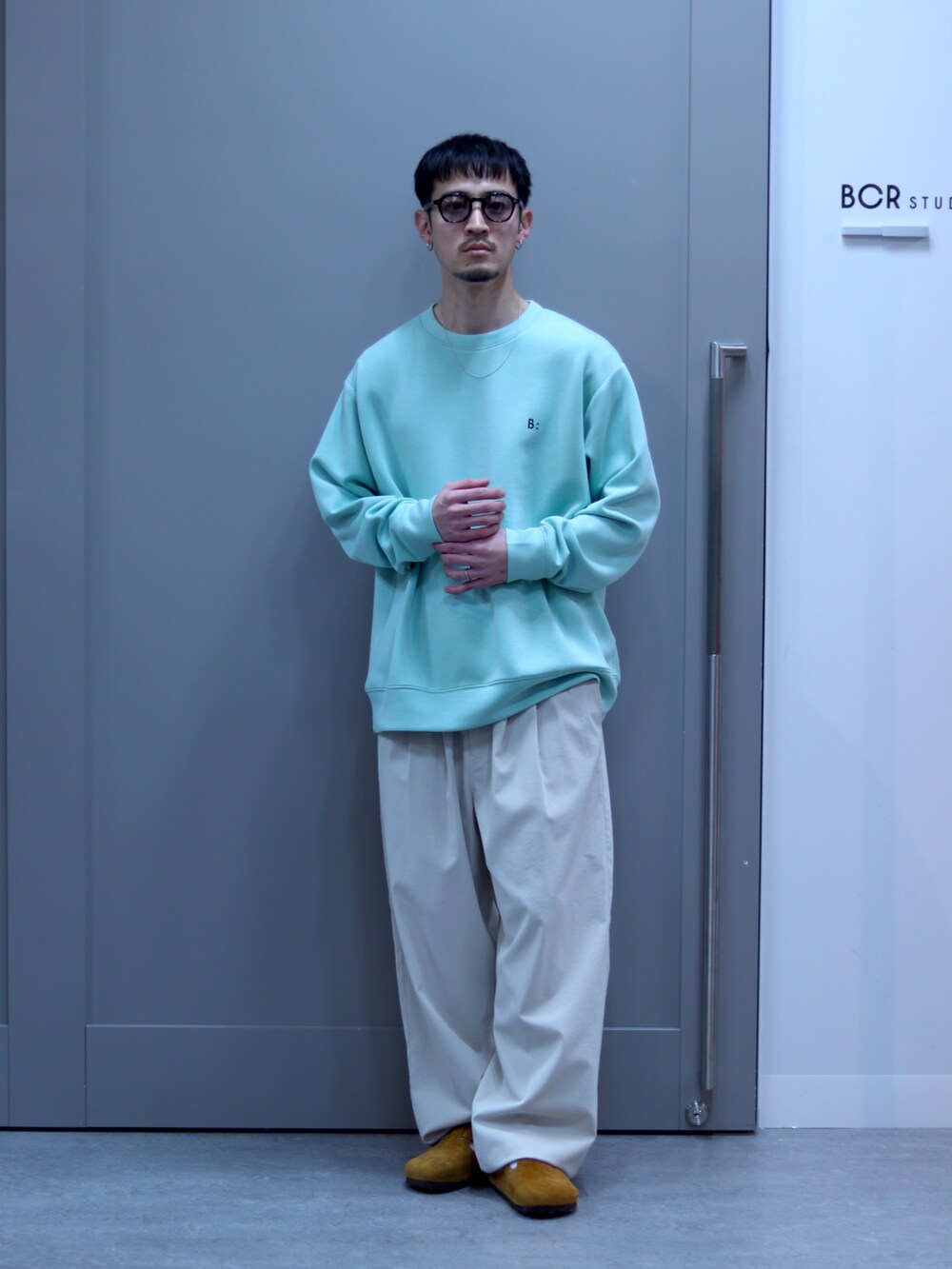 グリーン系のスウェット、ホワイト系のチノパンツ、ブラウン系のサングラスを着用したメンズの春コーディネートの2枚目の写真