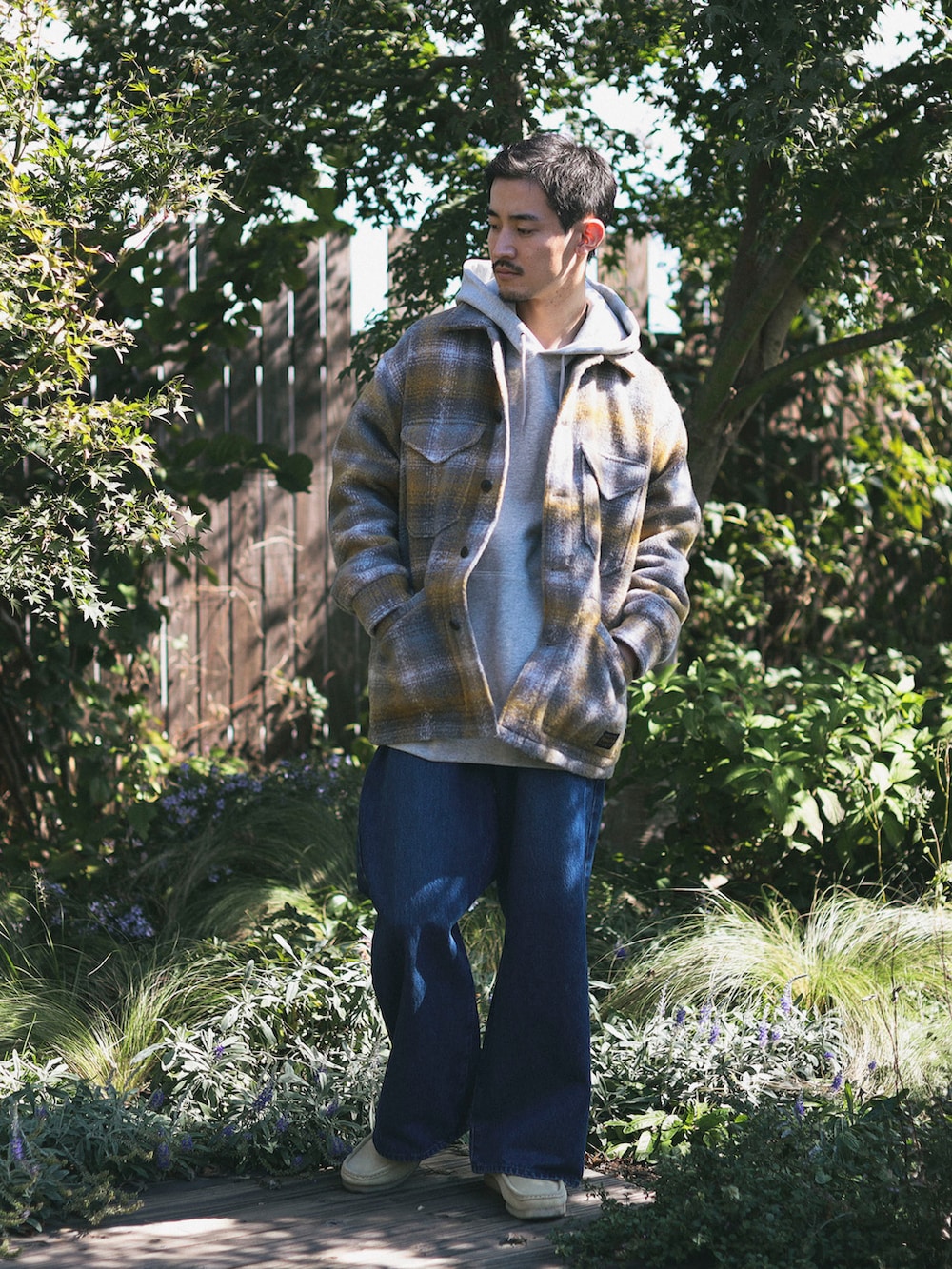 イエロー系のブルゾン、ブルー系のデニムパンツ、グレー系のパーカーを着用したメンズの秋コーディネートの2枚目の写真