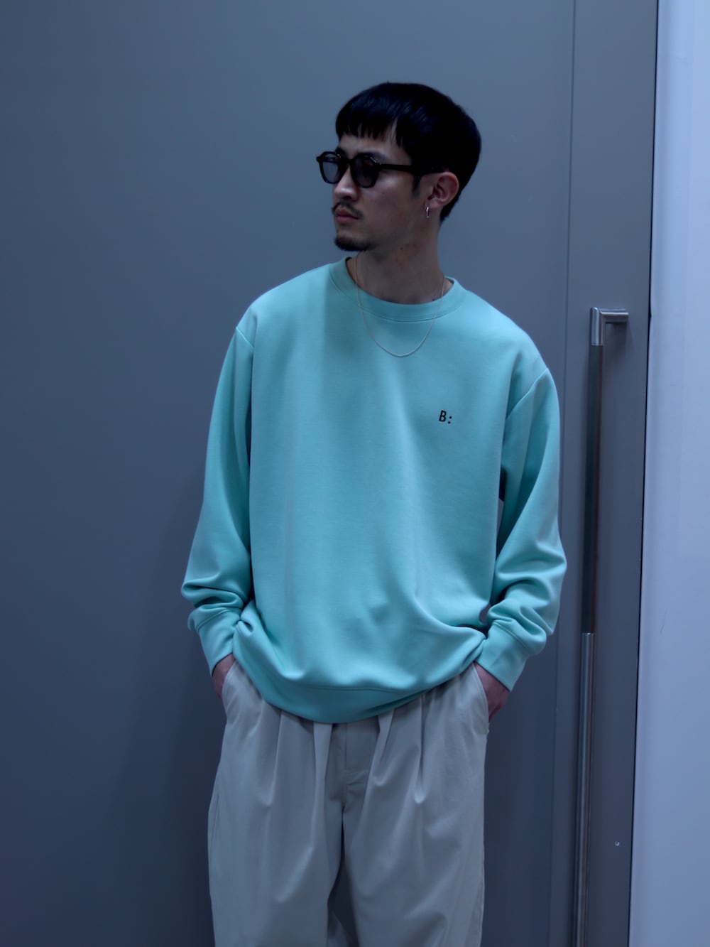 グリーン系のスウェット、ホワイト系のチノパンツ、ブラウン系のサングラスを着用したメンズの春コーディネートの3枚目の写真