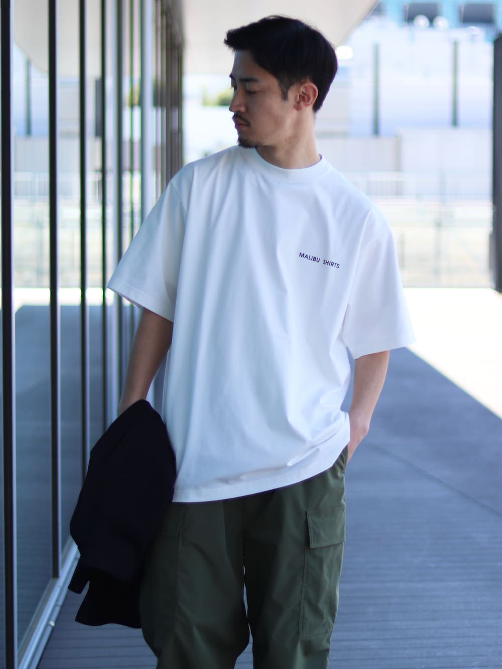 ホワイト系のTシャツ/カットソー、グリーン系のカーゴパンツ、ブラック系のスニーカーを着用したメンズの春コーディネートの2枚目の写真