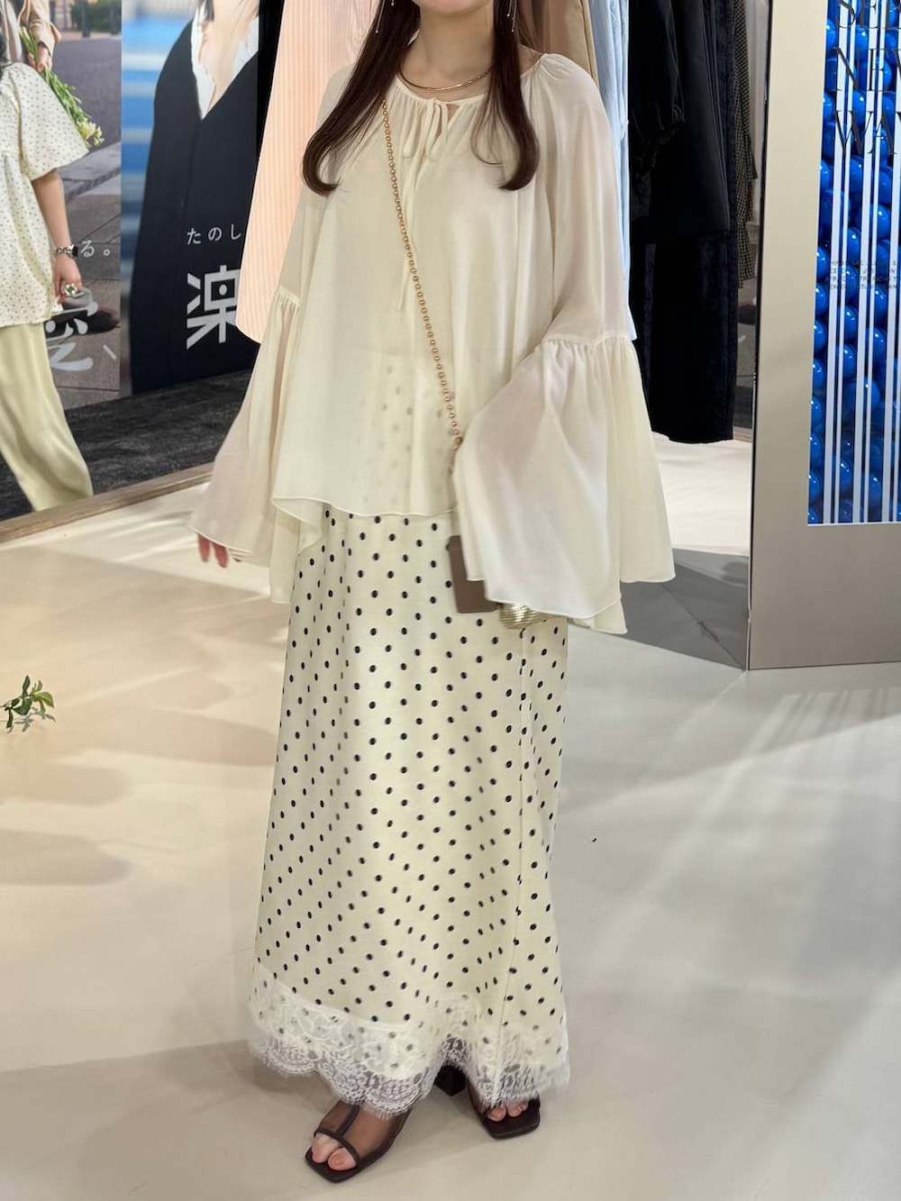 ゴールド系のショルダーバッグ、ブラウン系のサンダル、ホワイト系のスカートを着用したレディースの春コーディネートの2枚目の写真