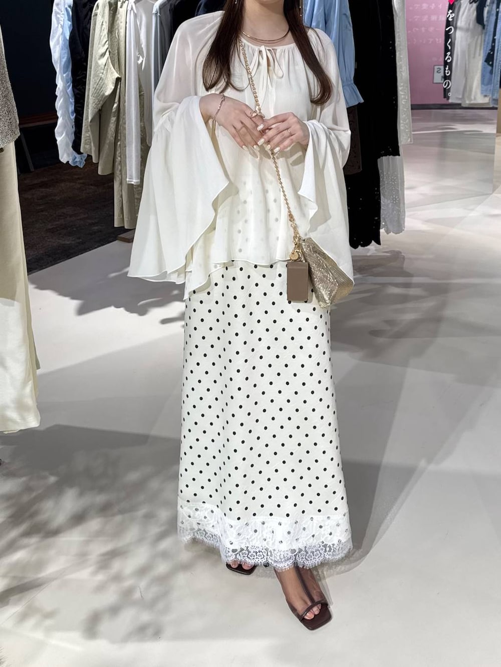 ゴールド系のショルダーバッグ、ブラウン系のサンダル、ホワイト系のスカートを着用したレディースの春コーディネートの2枚目の写真