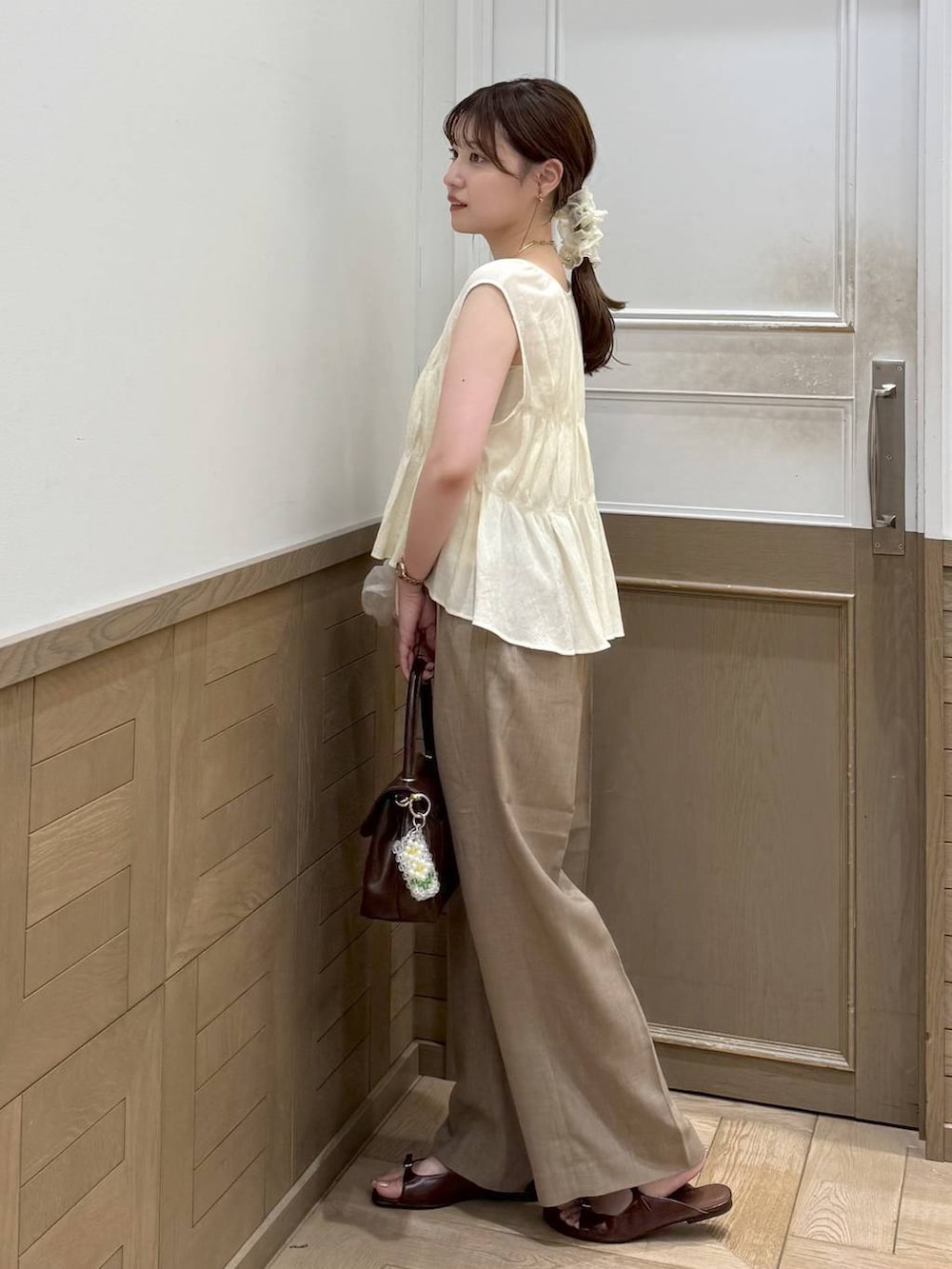 ベージュ系のスラックス、ブラウン系のサンダル、ブラウン系のボストンバッグを着用したレディースの夏コーディネートの2枚目の写真