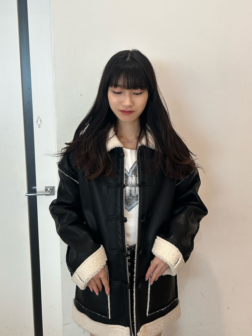 ブラック系のムートンコート、ホワイト系のTシャツ/カットソー、ブラック系のデニムパンツを着用したレディースの夏コーディネートの2枚目の写真