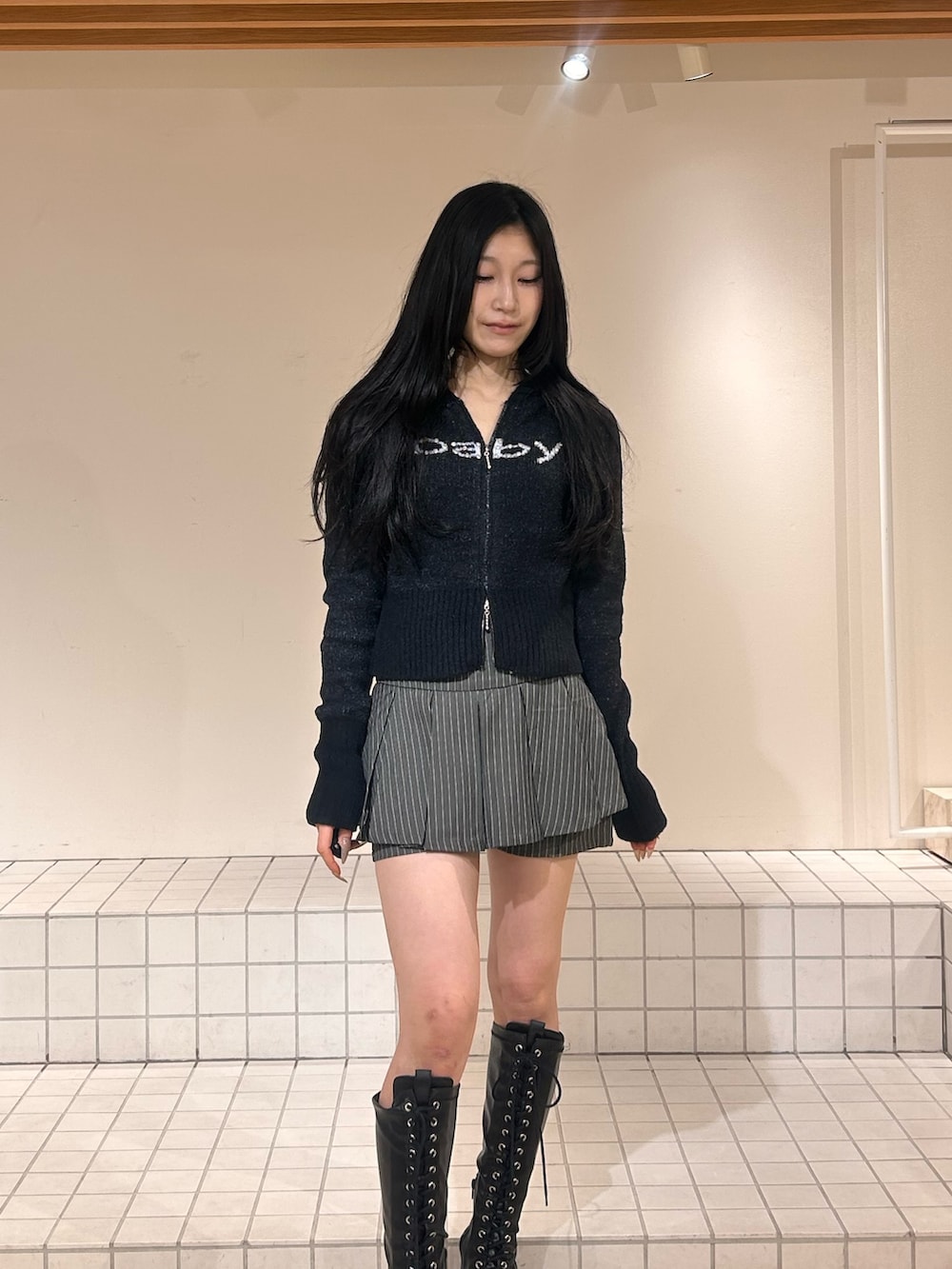 ブラック系のパーカー、グレー系のスカート、ブラック系のブーツを着用したレディースの冬コーディネートの4枚目の写真