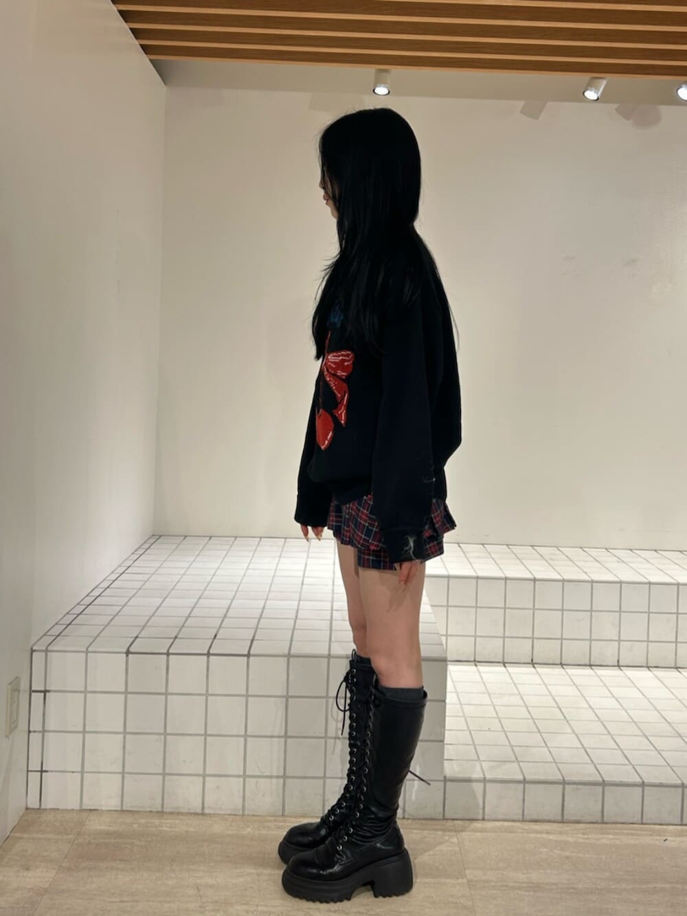 ブラック系のブーツ、ブラック系のニット/セーター、ブルー系のスカートを着用したレディースの秋コーディネートの2枚目の写真