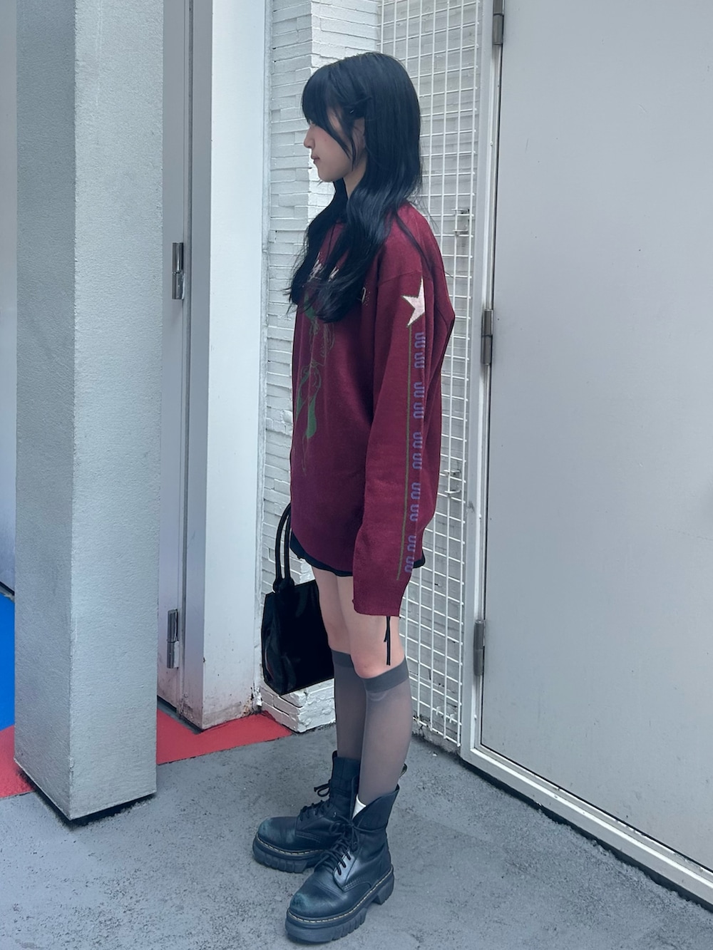 レッド系のニット/セーター、ブラック系のスカート、ブラック系のチョーカーを着用したレディースの秋コーディネートの2枚目の写真