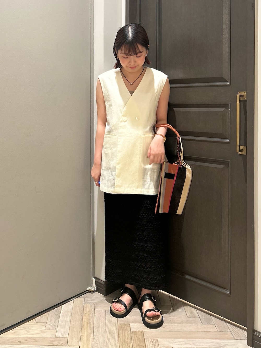 グレー系のキャミソール、ホワイト系のノーカラージャケット、ブラック系のスカートを着用したレディースの秋コーディネートの2枚目の写真