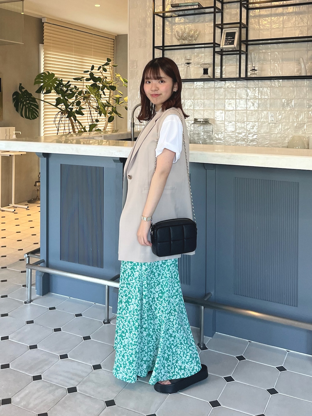 ベージュ系のベスト、グリーン系のスカート、ブラック系のショルダーバッグを着用したレディースの夏コーディネートの2枚目の写真