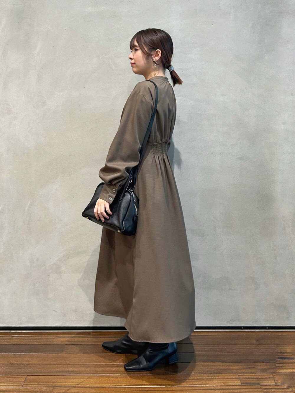 ブラウン系のワンピース、ブラック系のハンドバッグ、ブラック系のブーツを着用したレディースの冬コーディネートの2枚目の写真