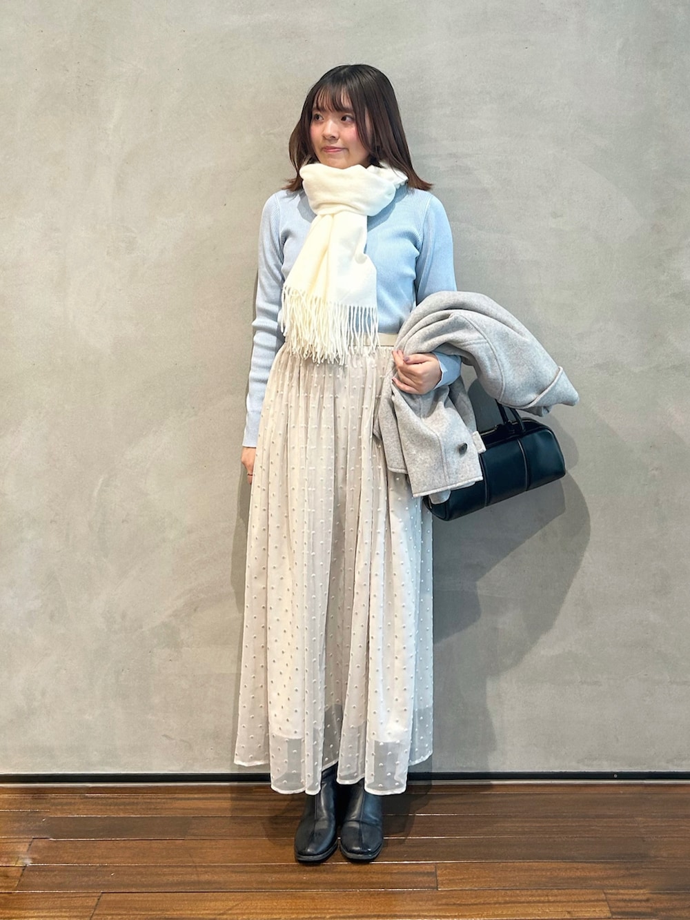 グレー系のステンカラーコート、ブルー系のカーディガン/ボレロ、ホワイト系のスカートを着用したレディースの冬コーディネートの2枚目の写真