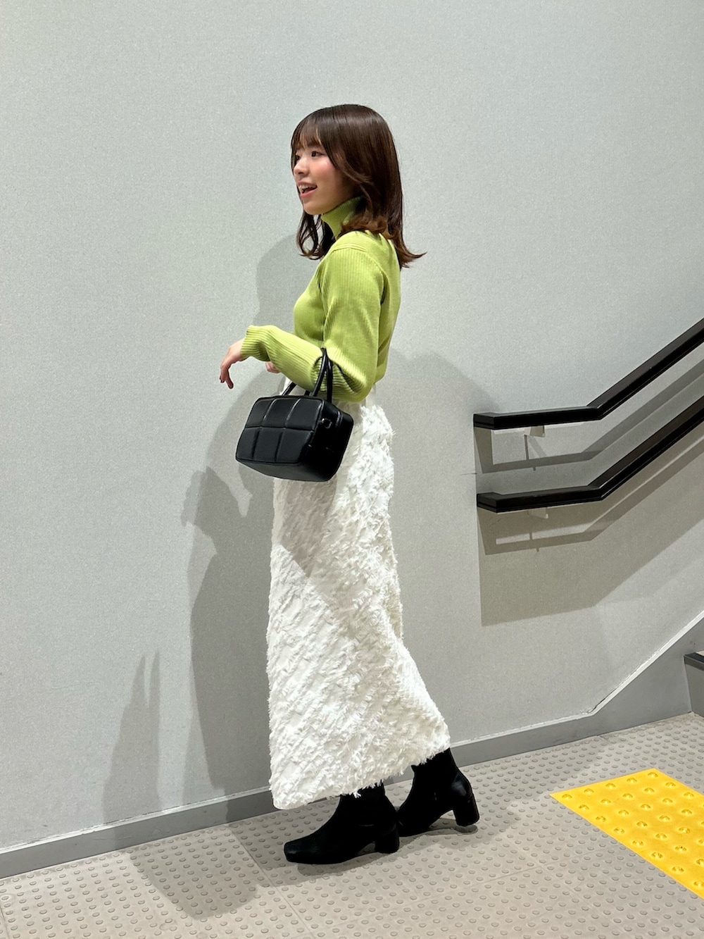 グリーン系のニット/セーター、ホワイト系のスカート、ブラック系のボストンバッグを着用したレディースの冬コーディネートの2枚目の写真