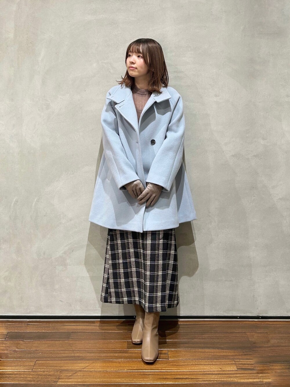 ブルー系のステンカラーコート、ブラック系のスカート、ブラウン系のニット/セーターを着用したレディースの冬コーディネートの2枚目の写真