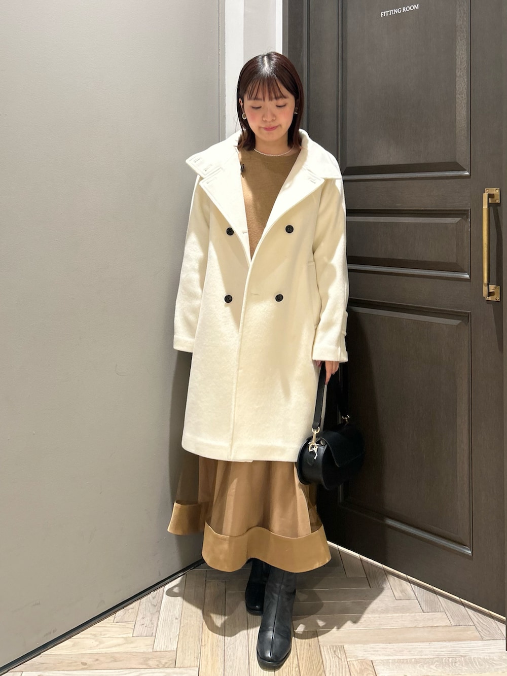 ホワイト系のその他アウター、ベージュ系のワンピース、ブラック系のハンドバッグを着用したレディースの冬コーディネートの2枚目の写真