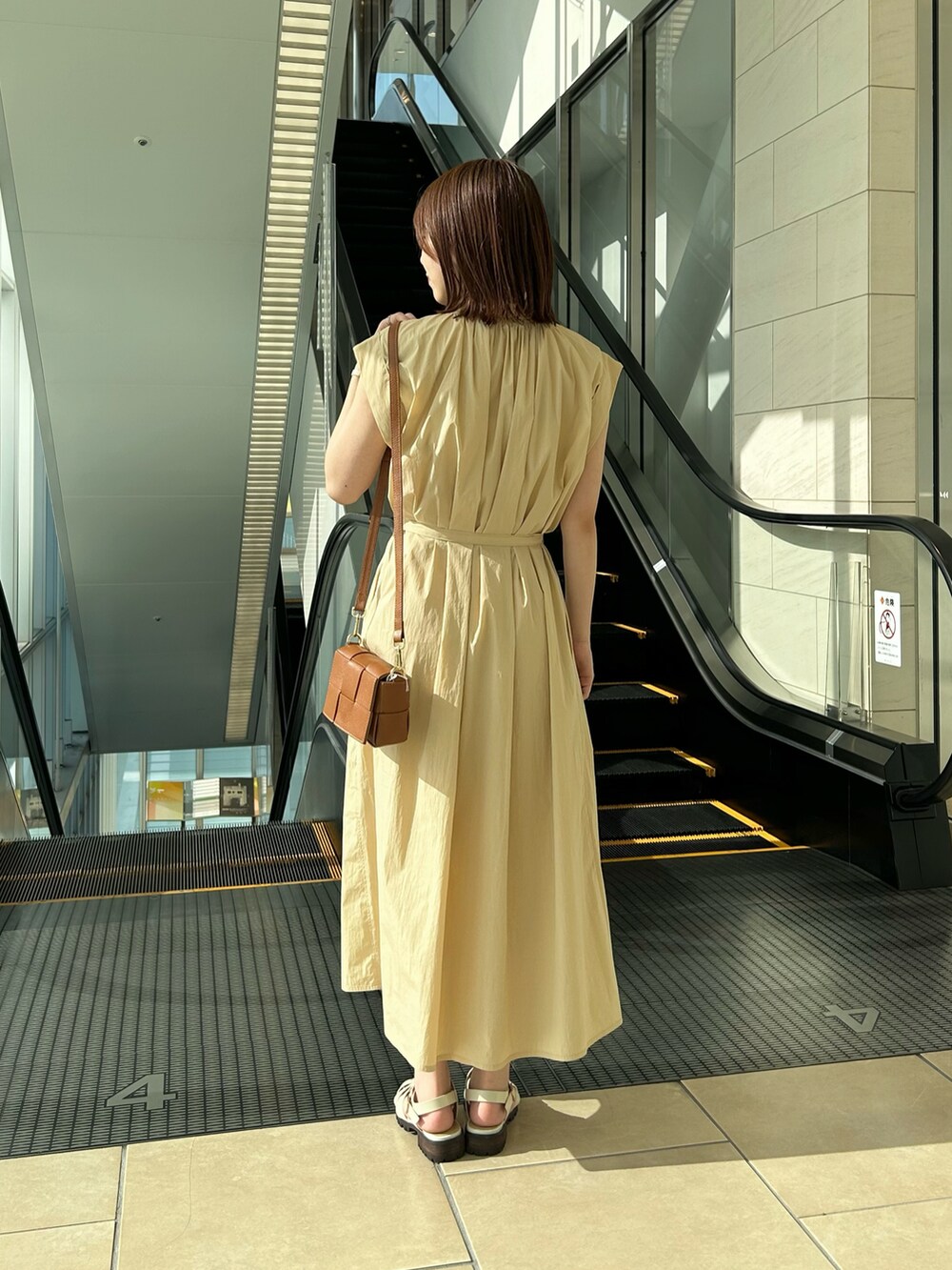 イエロー系のワンピース、ブラック系のショルダーバッグ、ホワイト系のサンダルを着用したレディースの夏コーディネートの3枚目の写真