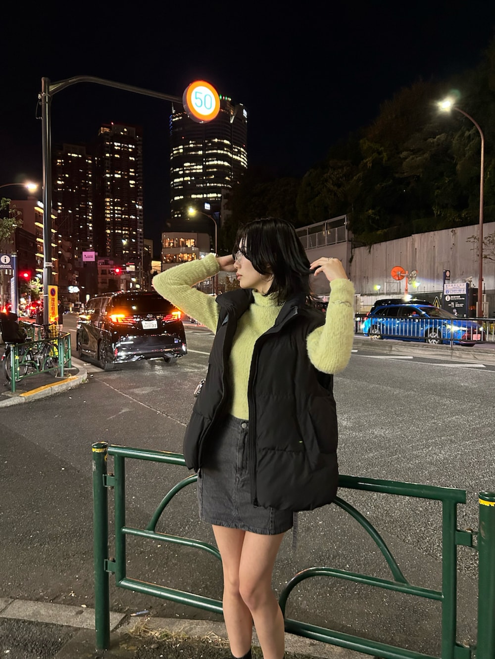 グリーン系のニット/セーター、グレー系のスカート、ブラック系のダウンベストを着用したレディースの秋コーディネートの2枚目の写真