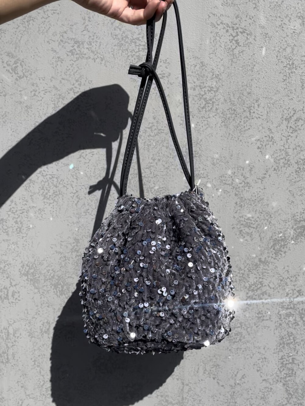 シルバー系のハンドバッグ、ベージュ系のベスト、ブラック系のサンダルを着用したレディースの夏コーディネートの3枚目の写真