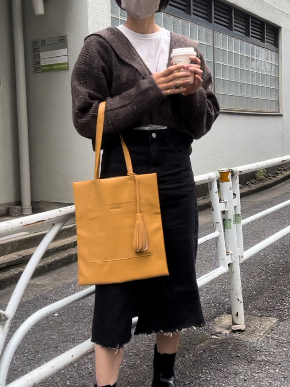 イエロー系のトートバッグ、ブラウン系のカーディガン/ボレロ、ブラック系のデニムスカートを着用したレディースの秋コーディネートの3枚目の写真