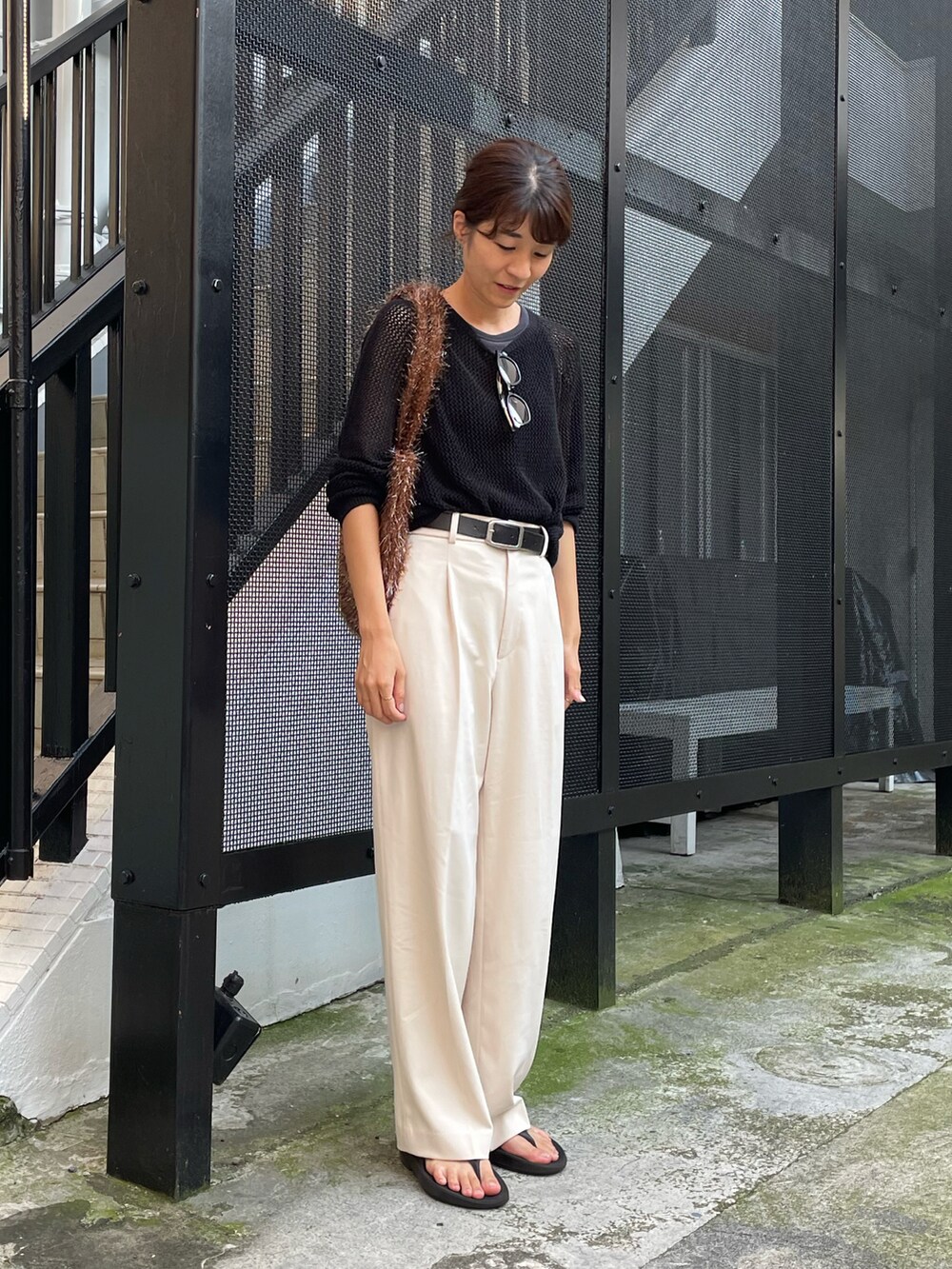 ブラウン系のトートバッグ、ホワイト系のパンツ、ブラック系のサンダルを着用したレディースの夏コーディネートの2枚目の写真