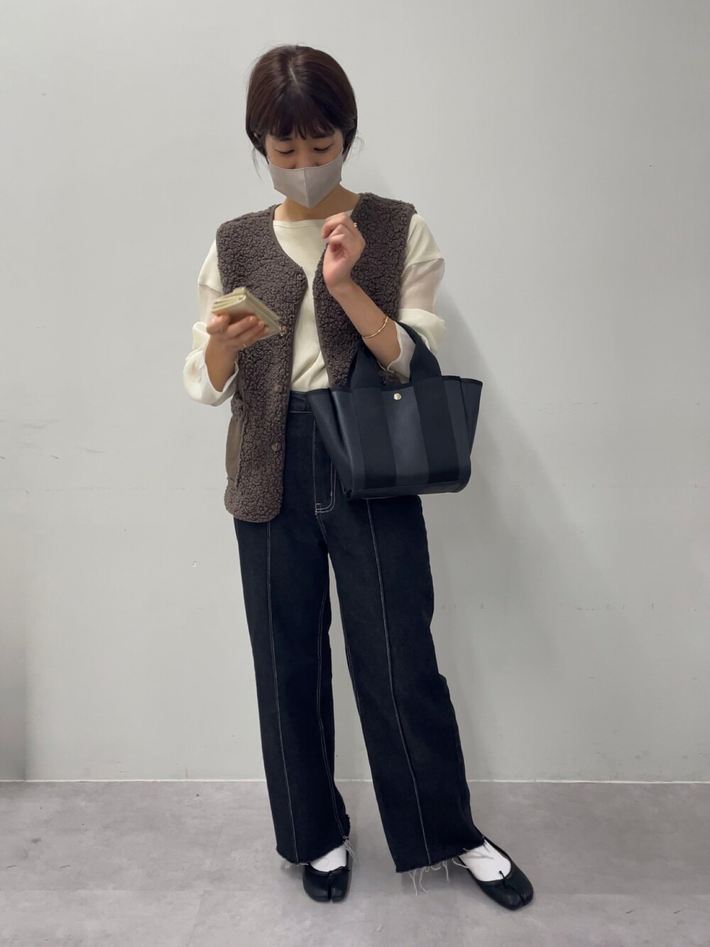 ブラック系のトートバッグ、ブラウン系のベスト、ベージュ系のTシャツ/カットソーを着用したレディースの秋コーディネートの3枚目の写真