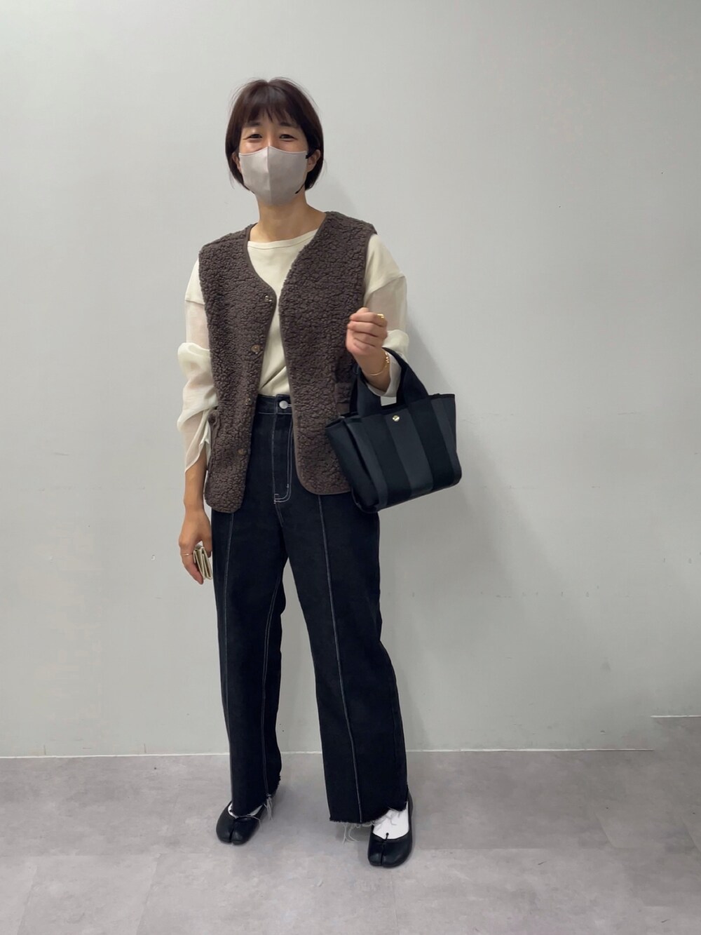 ブラック系のトートバッグ、ブラウン系のベスト、ベージュ系のTシャツ/カットソーを着用したレディースの秋コーディネートの2枚目の写真