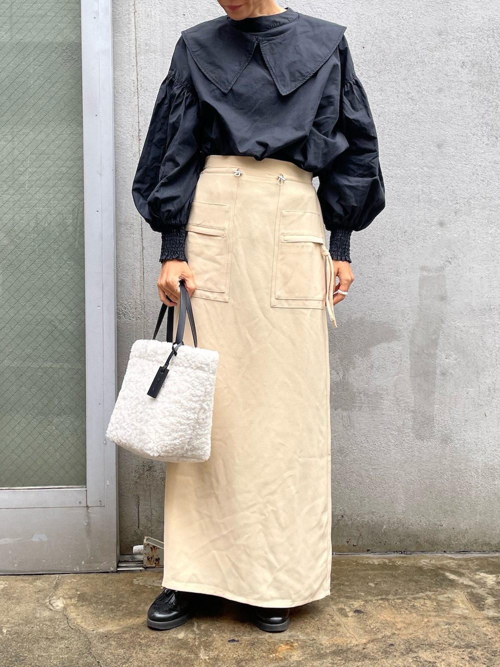 ホワイト系のトートバッグ、ベージュ系のスカート、ブラック系のシャツ/ブラウスを着用したレディースの秋コーディネートの2枚目の写真
