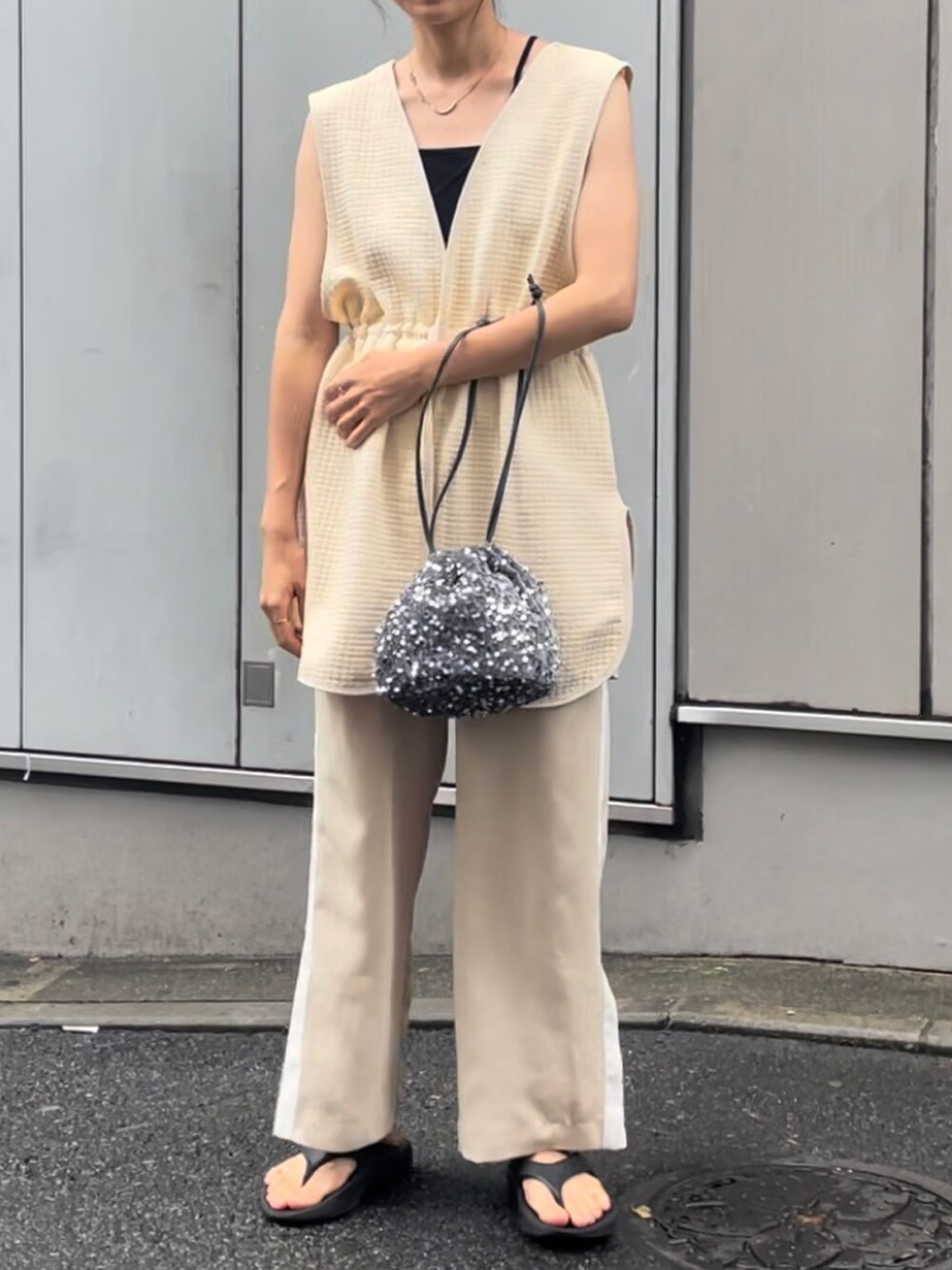 シルバー系のハンドバッグ、ベージュ系のベスト、ブラック系のサンダルを着用したレディースの夏コーディネートの2枚目の写真