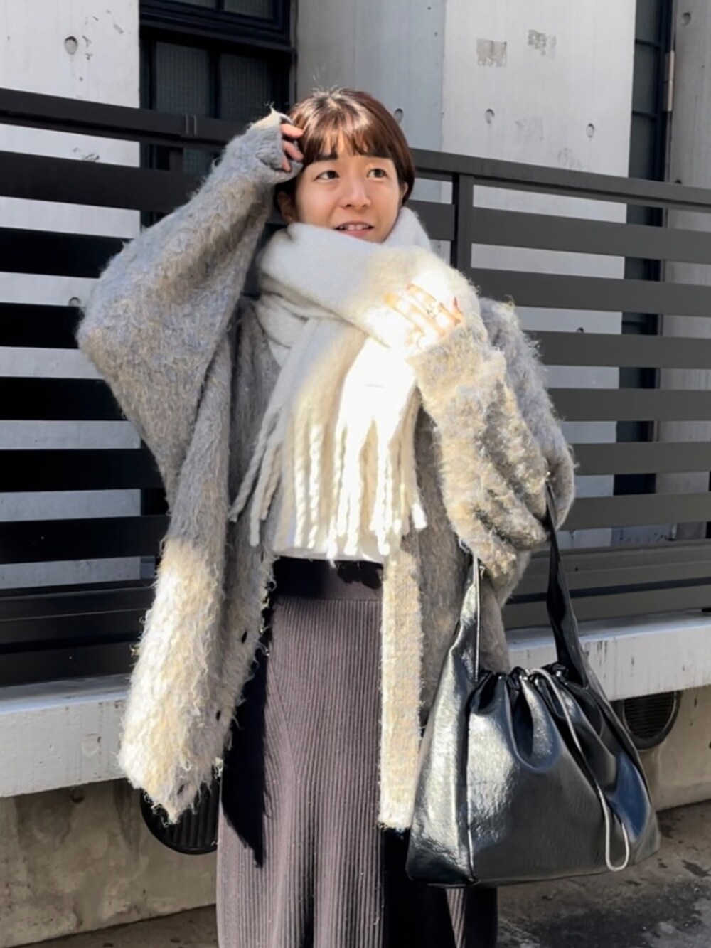 グレー系のカーディガン/ボレロ、ブラック系のスカート、ホワイト系のストール/ショールを着用したレディースの冬コーディネートの2枚目の写真