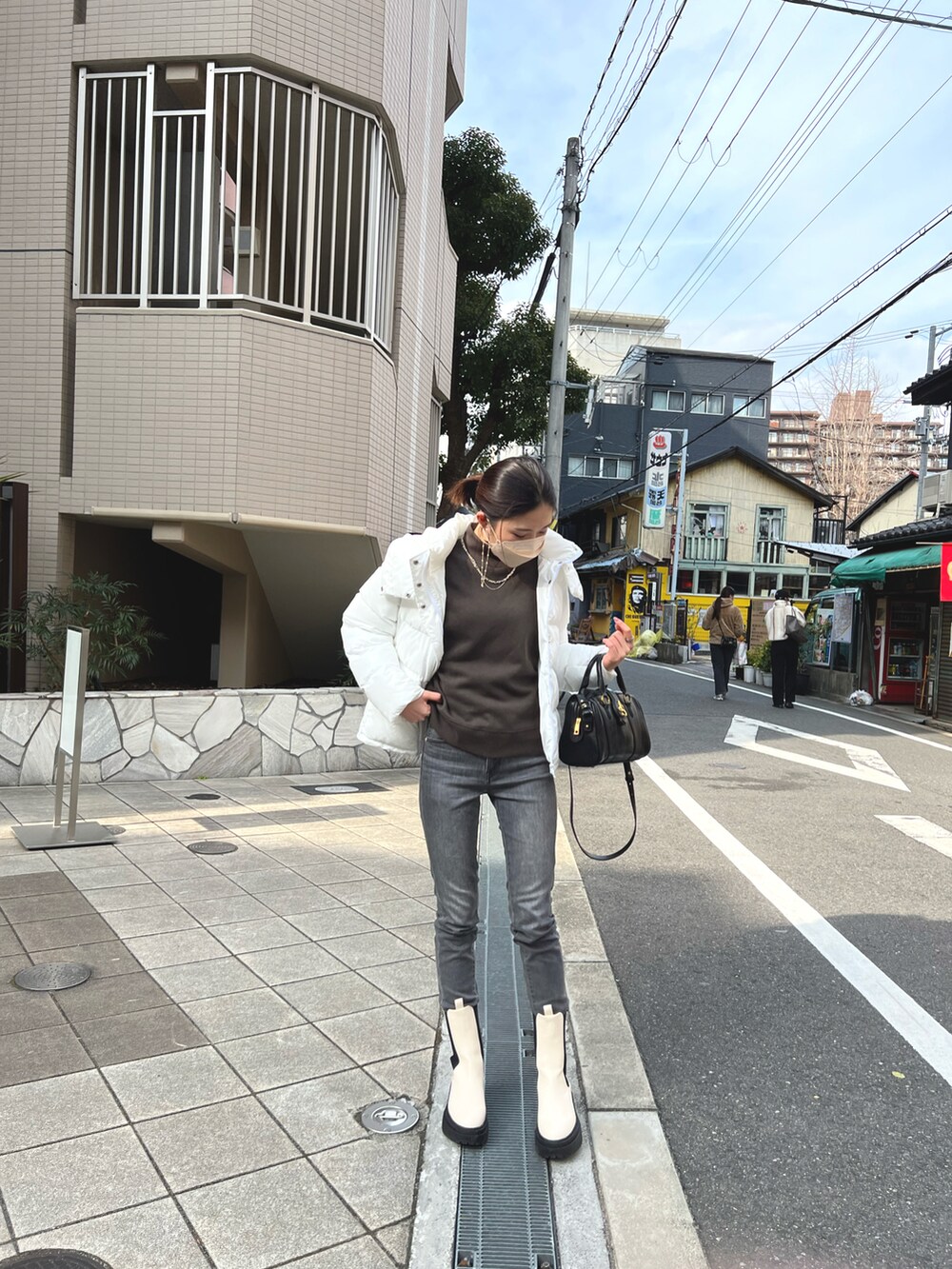 ホワイト系のブーツ、ブラック系のハンドバッグ、グレー系のデニムパンツを着用したレディースの冬コーディネートの2枚目の写真