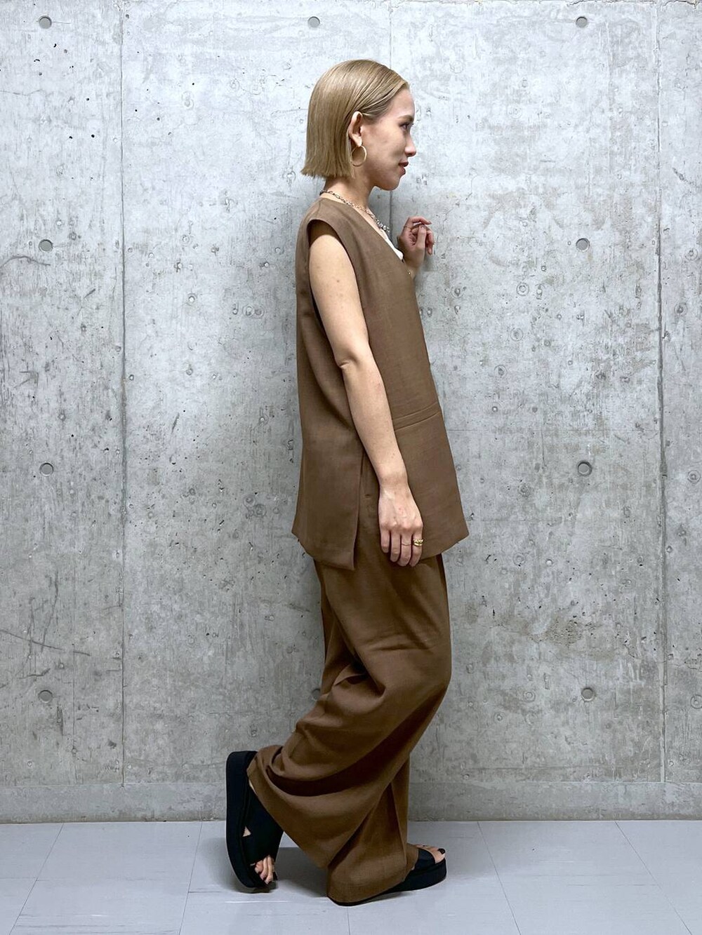 ブラウン系のベスト、ブラウン系のスラックス、ブラック系のサンダルを着用したレディースの夏コーディネートの2枚目の写真