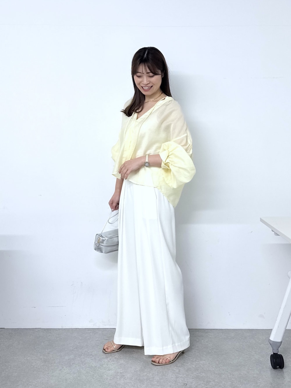 イエロー系のシャツ/ブラウス、ホワイト系のスラックス、シルバー系のトートバッグを着用したレディースの春コーディネートの2枚目の写真